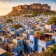 Jodhpur Blue City in Rajasthan showcasing rows of blue-painted houses and narrow streets with Mehrangarh Fort towering above, captured in warm daylight with vibrant colors and detailed cityscape.