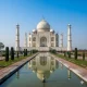 “Taj Mahal in Agra, white marble monument reflecting in the Yamuna River under a clear blue sky”