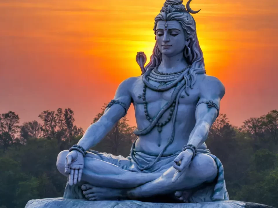 Meditating Lord Shiva statue seated in Padmasana on a tiger skin pedestal, with a glowing orange sunset sky in the background, symbolizing peace, spirituality, and divine power.